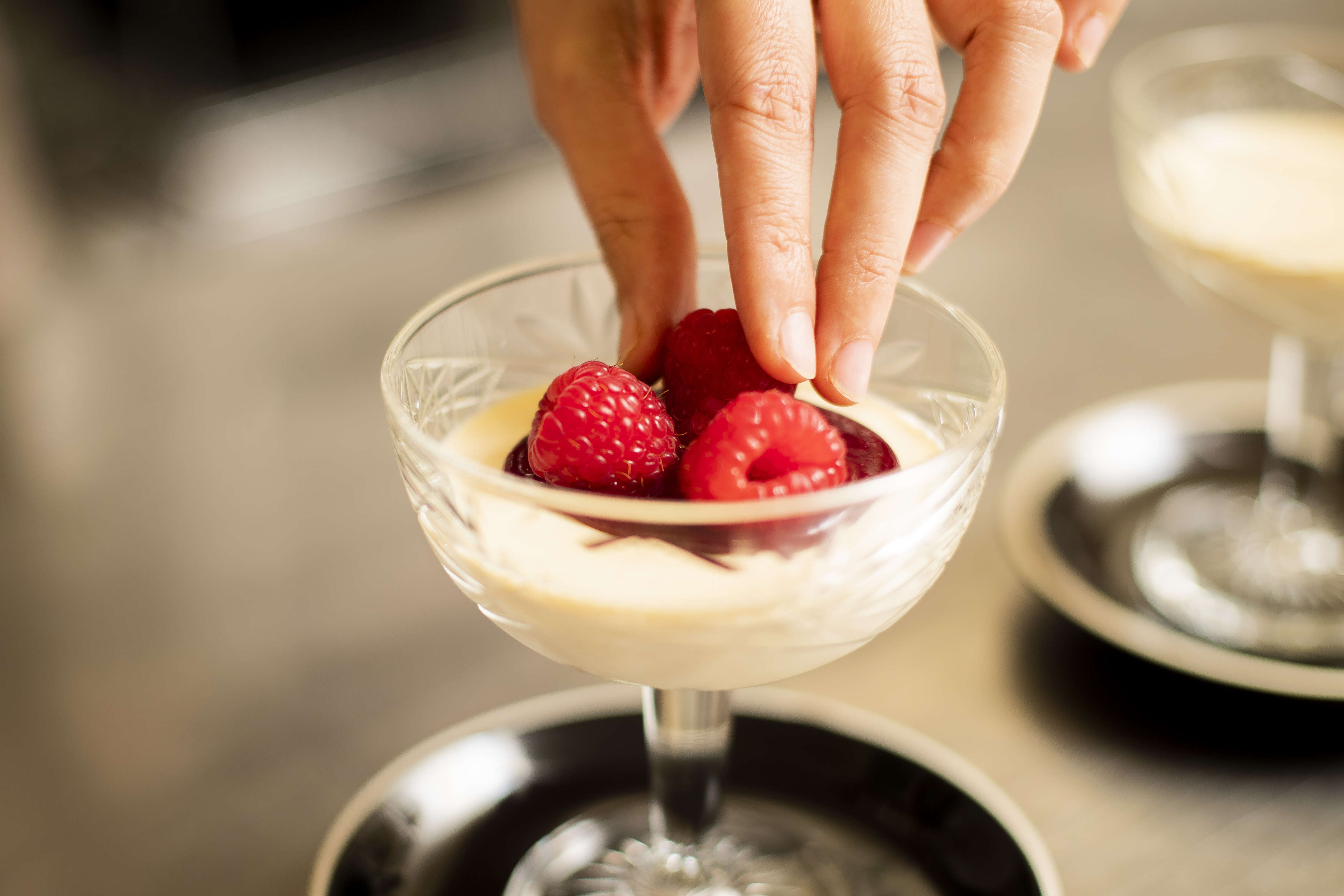 Vanilla panna cotta with raspberry coulis and fresh raspberries being placed on top. Photo: Richard Jupe.