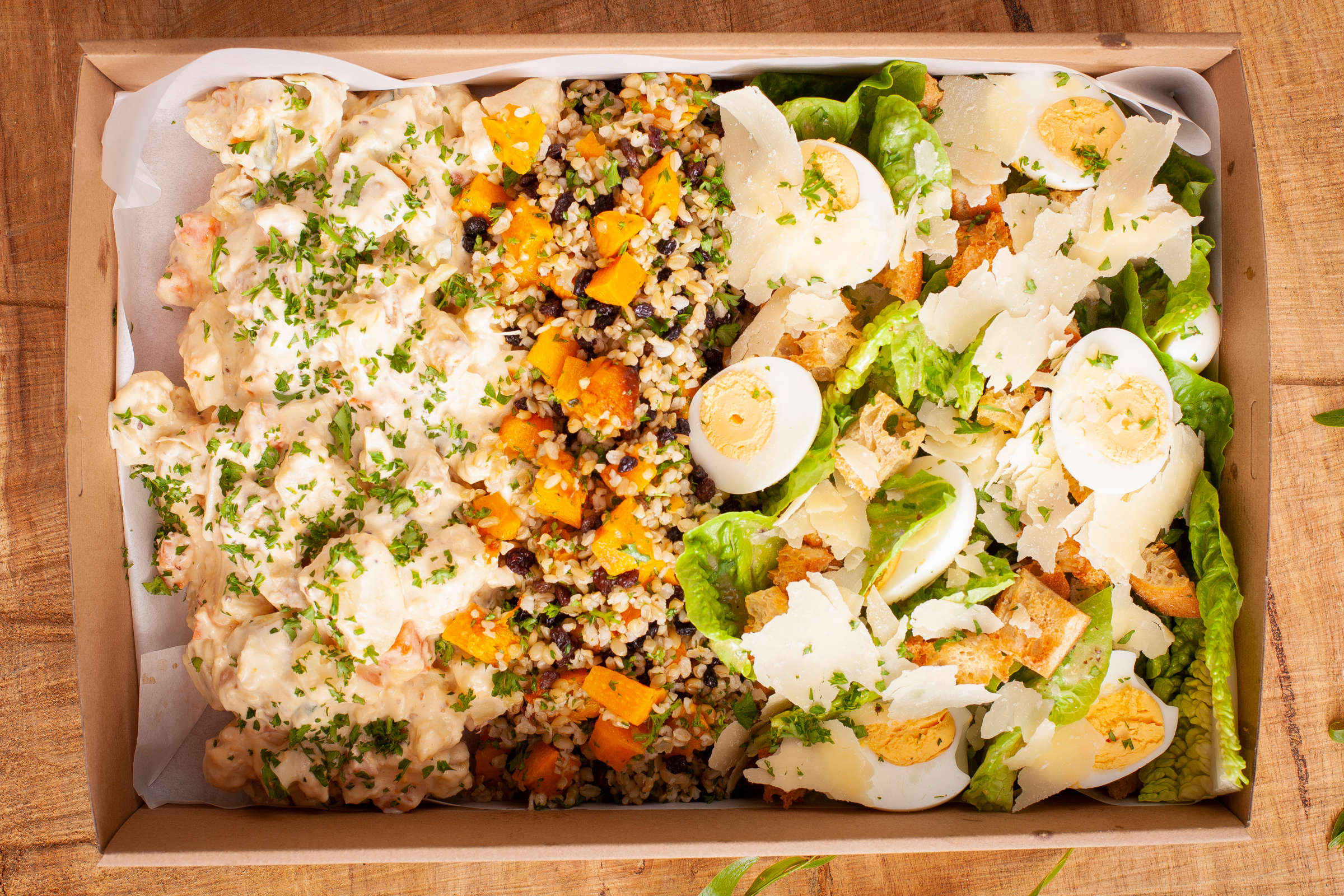 Mixed salad catering box. Salads included are (1) cos salad with croutons, hard boiled eggs, Caesar dressing, and parmesan; (2) roast pumpkin, currant, fresh herbs and freekeh; (3) potato salad with a mustard mayonnaise dressing. Credit: Richard Jupe.